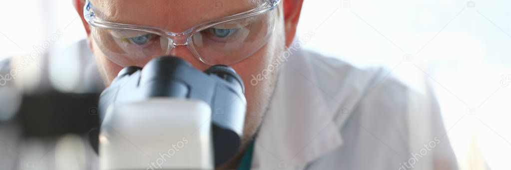 Portrait of a young chemist looking in binocular