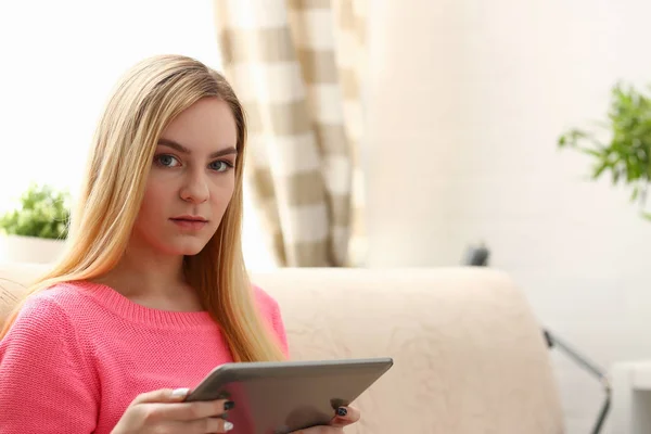 Jovem bela mulher loira sentar-se no sofá na sala de estar segurar tablet nos braços — Fotografia de Stock