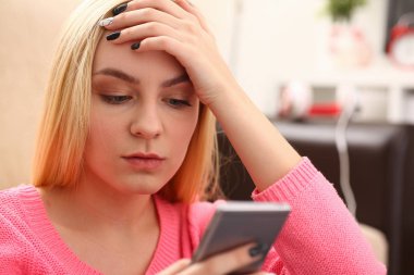 Genç sarışın womansit kanepe tutun Smartphone elinde güzel