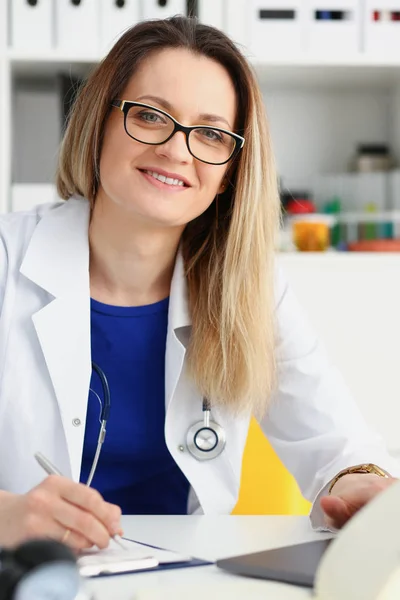 Schön lächelnde Ärztin sitzt am Arbeitsplatz — Stockfoto