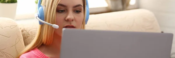 young beautiful blond woman sit on the sofa in livingroom hold laptop in arms listen to music