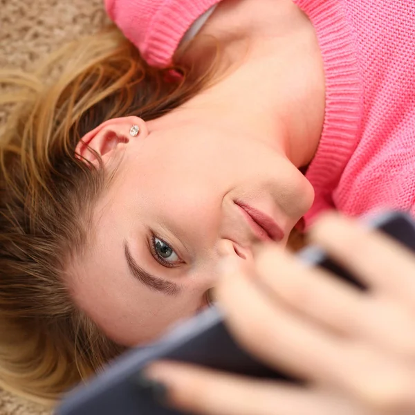 Молода красива жінка відпочиває лежить на підлозі тримає смартфон в руках — стокове фото