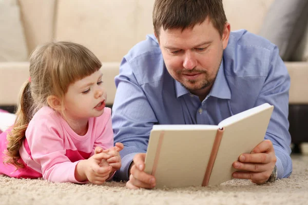 Far och dotter ligga på golvet läsning intressant bok — Stockfoto