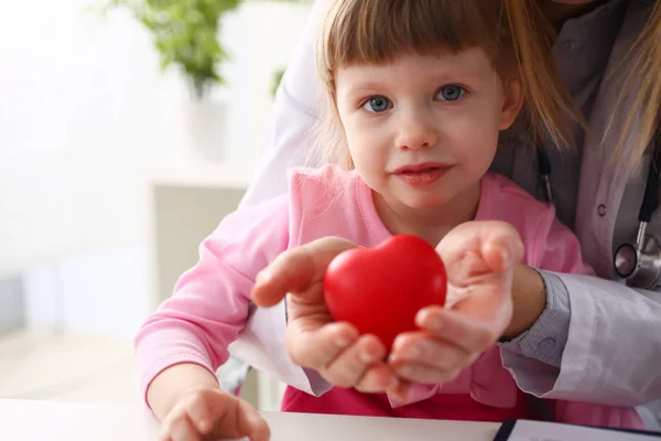 작은 아기 소녀 방문 의사 지주 손에 빨간 장난감 심장 — 스톡 사진