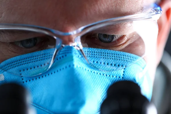Erkek laboratuvar çalışanı gözleri koruyucu maske takan mikroskop bakıyor — Stok fotoğraf