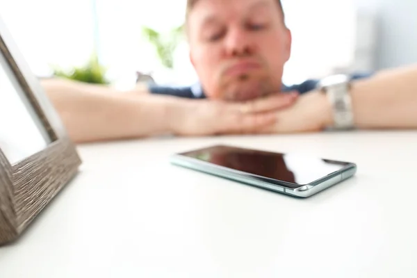 Celular deitado na mesa com o homem pensativo no fundo à espera de chamada — Fotografia de Stock