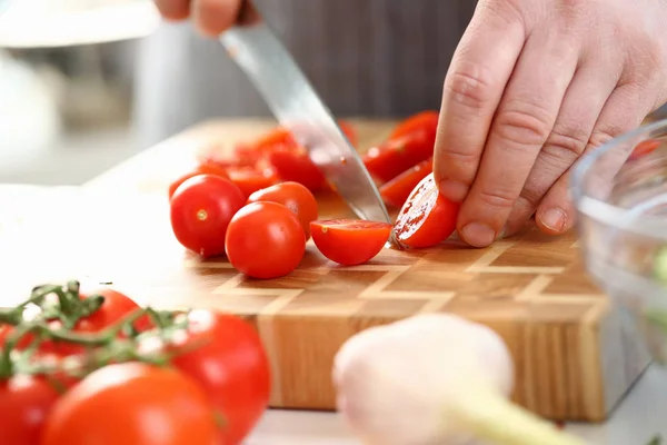 Mãos masculinas que cortam o ingrediente maduro do tomate cereja — Fotografia de Stock