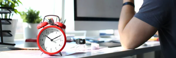 Reloj despertador rojo en la mesa de trabajo con un hombre reflexivo — Foto de Stock