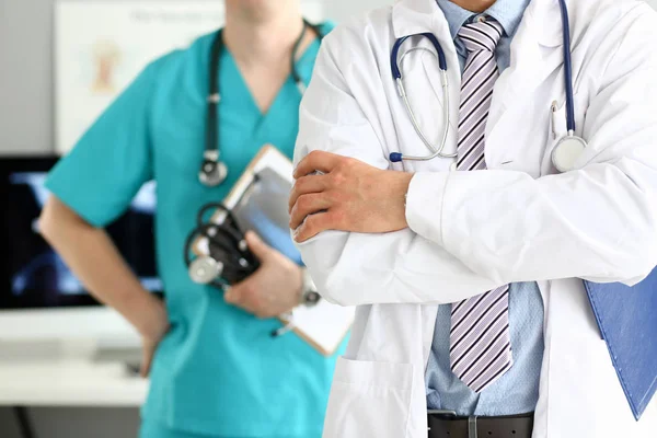 Médico masculino con los brazos cruzados en el pecho de pie en línea con sus colegas en el consultorio — Foto de Stock