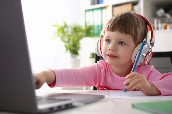 小さな女の子の身に着けているヘッドフォンは、モバイル コンピューターを使用してください。 — ストック写真