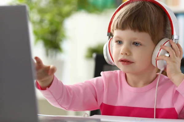 Kleines Mädchen mit Kopfhörern benutzt mobilen Computer — Stockfoto