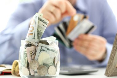 Büyük kavanoz para dolu kredi kartları demet tutan erkek el ile çalışma masasında standı