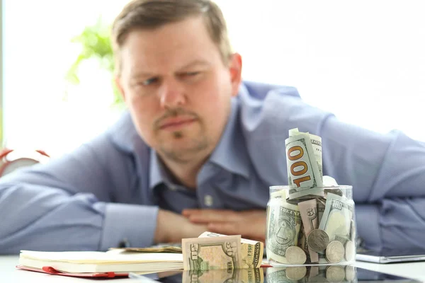 L'uomo che guarda il barattolo pieno di soldi pensando ai suoi debiti — Foto Stock