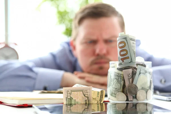 Hombre mirando frasco lleno de dinero pensando en sus deudas — Foto de Stock
