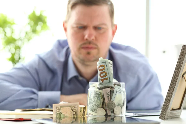 Hombre mirando frasco lleno de dinero pensando en sus deudas — Foto de Stock