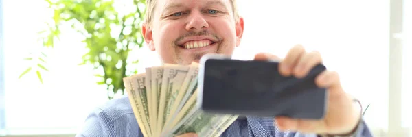 Человек делает самофото с камерой мобильного телефона, позируя с кучей денег — стоковое фото
