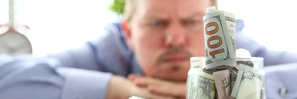 Hombre mirando frasco lleno de dinero pensando en sus deudas —  Fotos de Stock