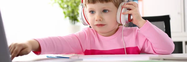 Kleines Mädchen mit Kopfhörern benutzt mobilen Computer — Stockfoto