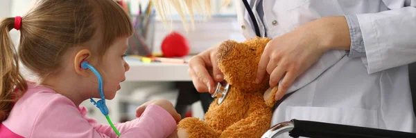 Menina segurar nos braços brinquedo estetoscópio jogando com ursinho de pelúcia — Fotografia de Stock