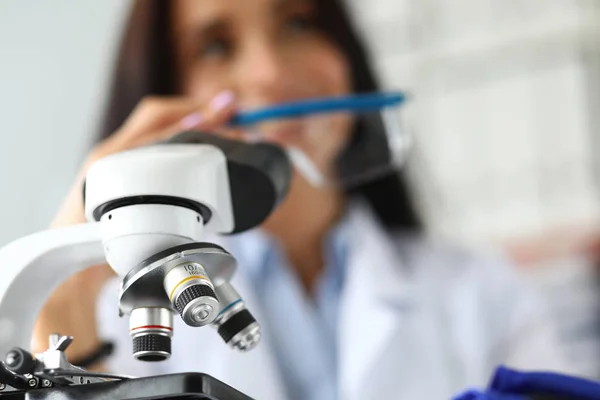 Lente de microscópio científico com analista feminina em segundo plano — Fotografia de Stock