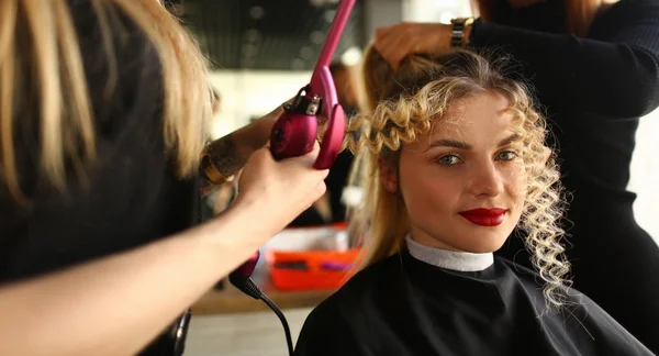 年轻女子获得卷曲的头发通过卷曲铁 — 图库照片