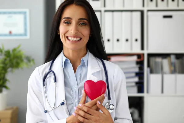 Schön lächelnder Hausarzt hält rotes Spielzeugherz in den Händen — Stockfoto