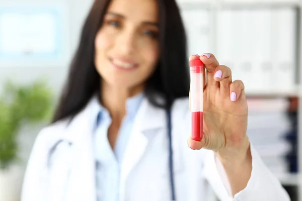 Médico femenino sosteniendo la mano tubo de ensayo de plástico que contiene líquido rojo — Foto de Stock