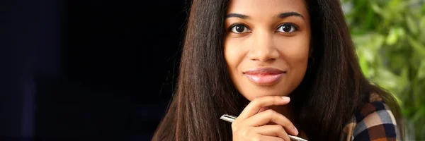 Negro sonriente mujer sentado en el lugar de trabajo mirando a la cámara — Foto de Stock