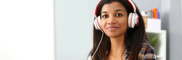 Preto sorrindo mulher sentada no local de trabalho usando fones de ouvido — Fotografia de Stock