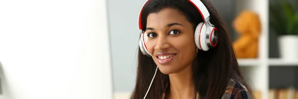 Black smiling woman sitting at workplace wearing headphones