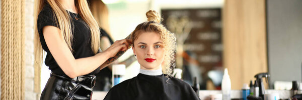 Руки парикмахера держат щипцы для завивки и делают
