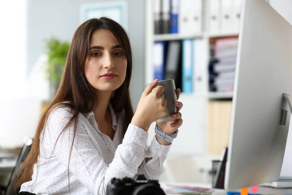 Mujer bastante adulta sentada en la mesa de trabajo bebiendo bebida caliente — Foto de Stock