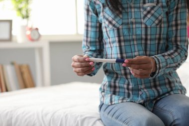 Yalnız bir kadın yatakta oturur ve hamilelik testi yapar.