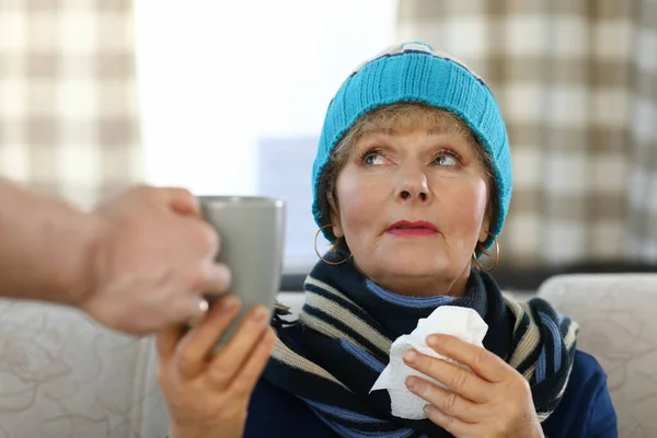 Ältere Frau mit Schal und Mütze sitzt auf Sofa — Stockfoto