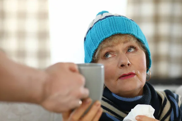 Грустная пожилая женщина дома берет чашку с горячим напитком — стоковое фото