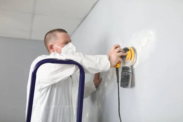 Male builder in uniform cleans wall with putty — Stock Image Male builder in uniform cleans wall with putty Royalty Free Stock Images