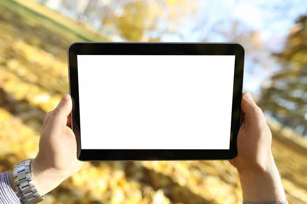 Homem fica no parque de outono e olha para tablet — Fotografia de Stock