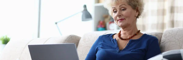 Пожилая женщина сидит с ноутбуком на коленях домой — стоковое фото