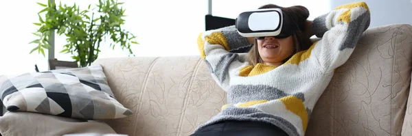 Chica se sienta sofá en casa se relaja con gafas virtuales —  Fotos de Stock