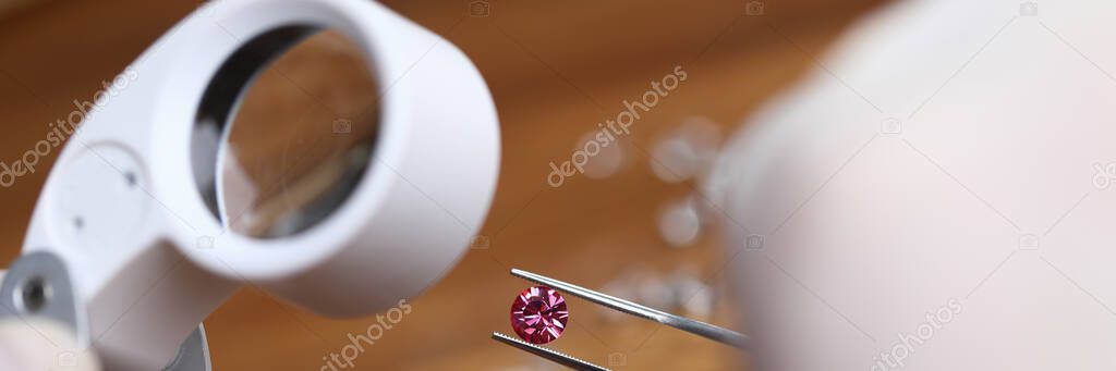 Jeweler examines red gem under magnifying glass