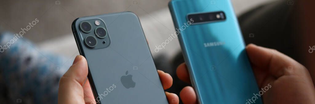 Minsk, Belarus - 11 December 2019 : Male hand hold Apple iphone pro and samsung galaxy s 10. Illustrative editorial