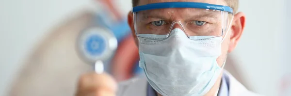 Médico masculino segurar na mão estetoscópio com coronavírus símbolo close-up . — Fotografia de Stock