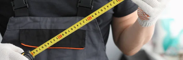 Repairman in uniform gloves measures tape measure