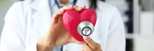 Hands of female GP holding stethoscope head near red toy heart — Stock Photo, Image