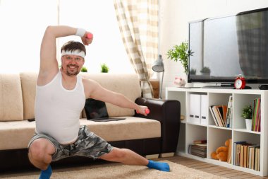 Neşeli genç adam evde dambıllarla egzersiz yapıyor.