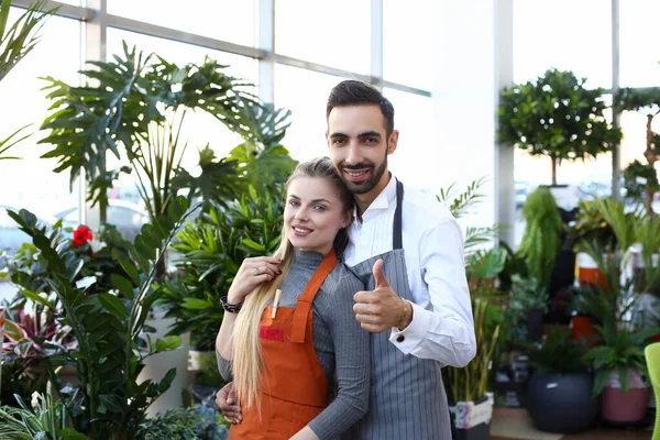 Happy young couple standing in flower shop — Stock Photo, Image