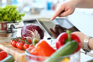 Genç adam taze salata pişiriyor ve tablet bilgisayar kullanıyor.