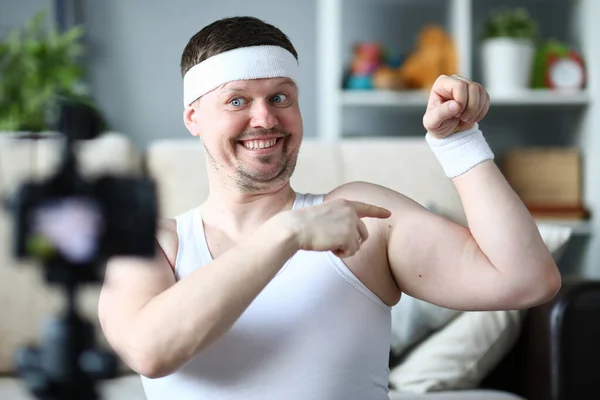 Veselý mladý ukazuje na své paže svaly při překódování videa — Stock fotografie