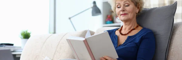 Пожилая женщина сидит дома на диване и читает книгу — стоковое фото