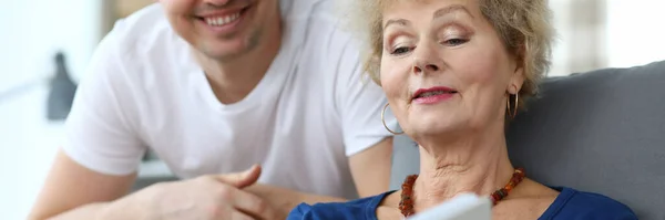 Пожилая леди сидит на диване и смотрит альбом со своим сыном — стоковое фото